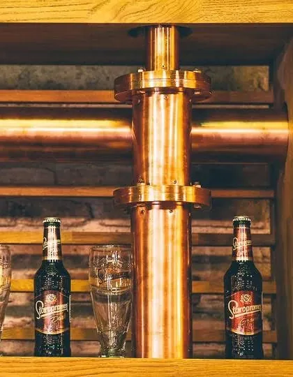 Sticle Staropramen și pahare pe raftul de lemn, lângă coloana de cupru
