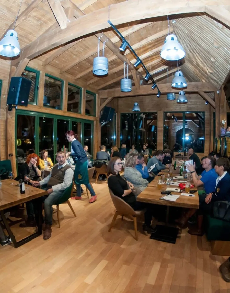 Sala cu grinzi de lemn, mese lungi și banchete verzi